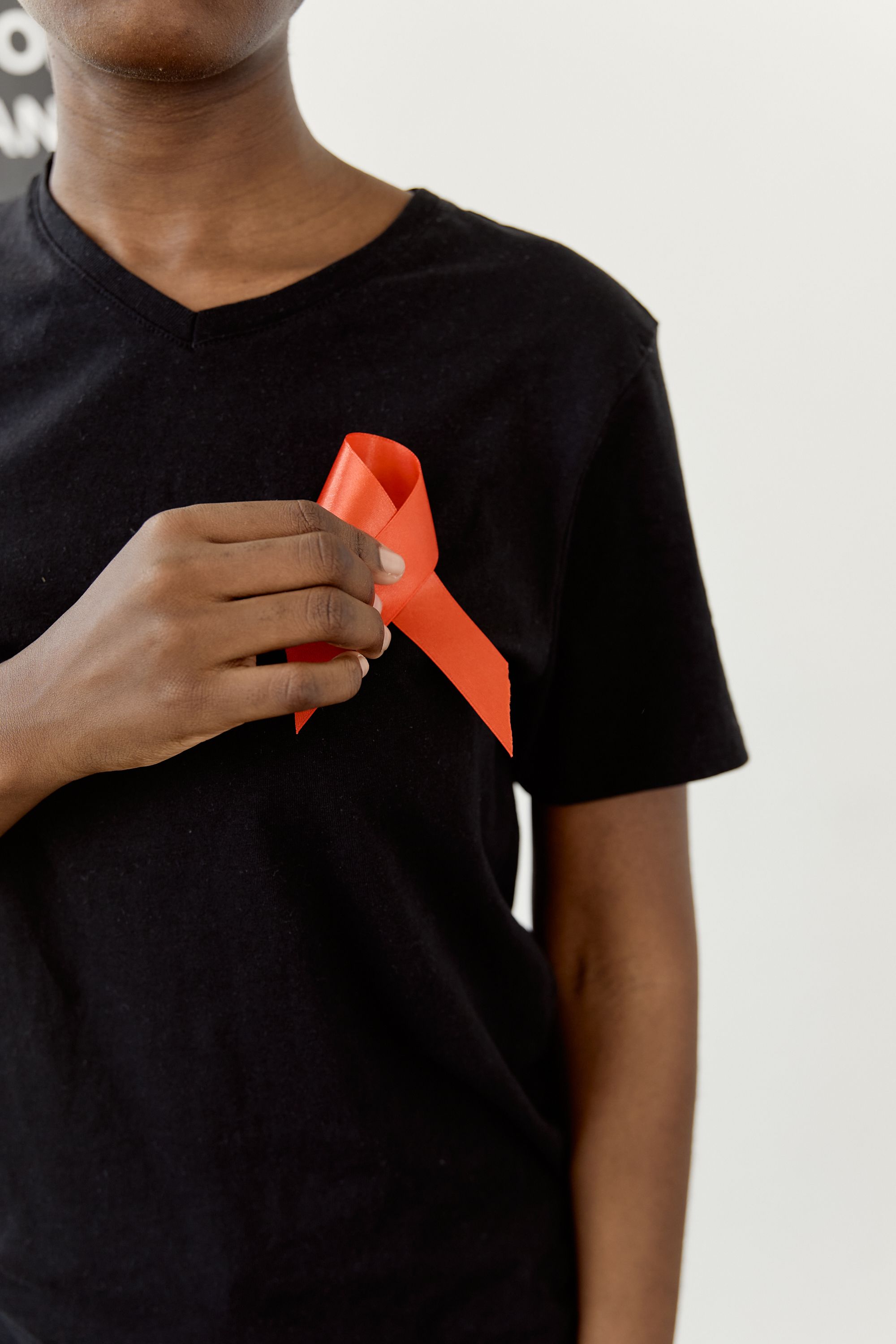 A person wearing a black shirt holds a red HIV awareness ribbon to their chest
